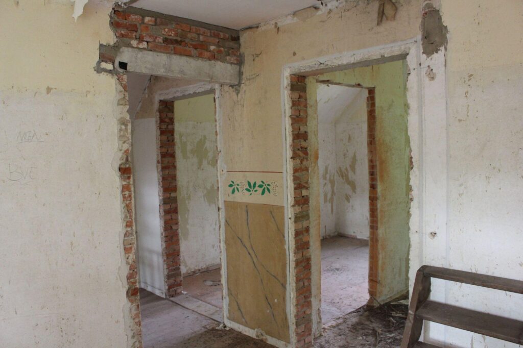 a photograph of a hallway in an abandoned building. there are four door openings that are wide open