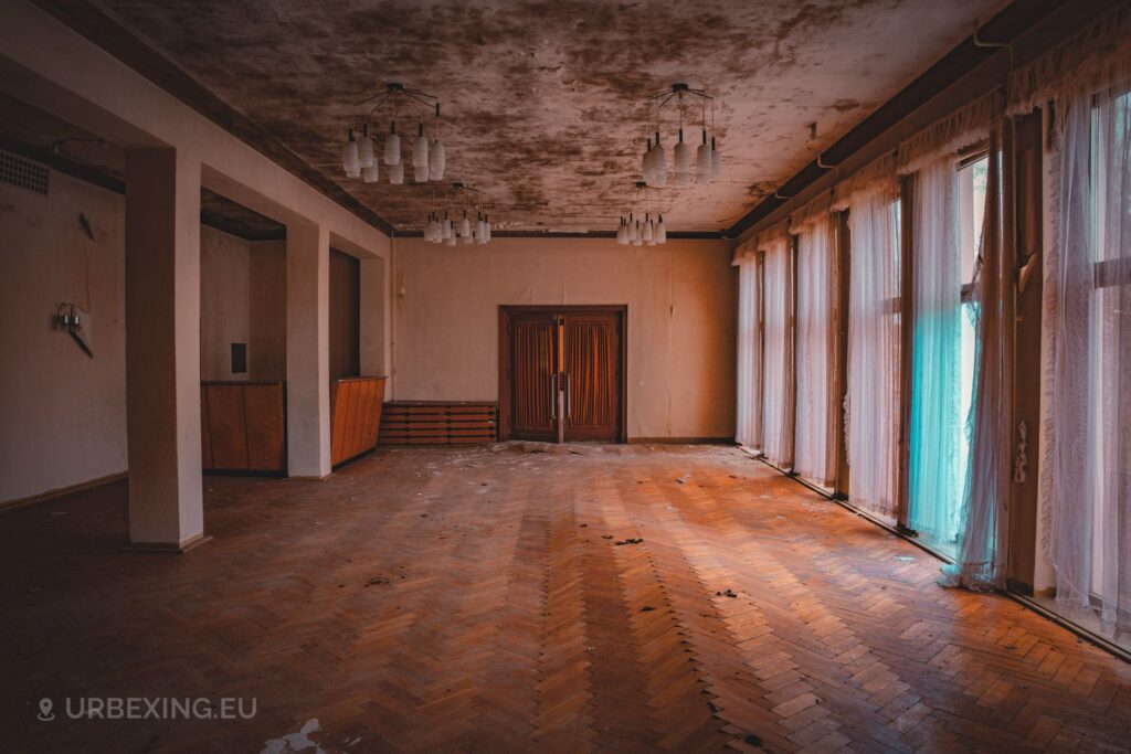 a photo of a hallway with double doors at the end, the floor and ceiling are decaying