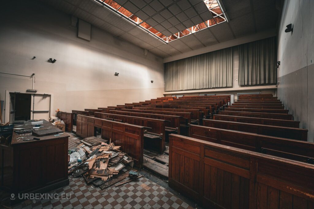 an empty auditorium filled with wooden benches for sutdents discovered during urbex