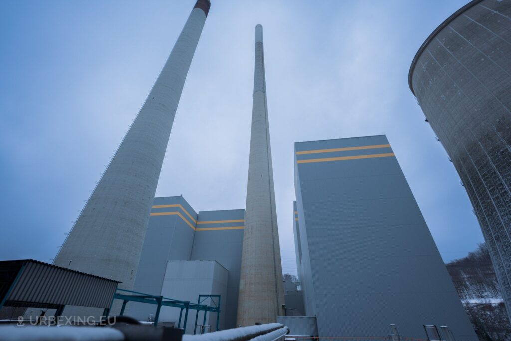 A picture of an abandoned power plant. The picture shows the chimneys, DeNOx buildings and the cooling tower. The buildings can be identified by their cubic structure, gray color and yellow stripes.
