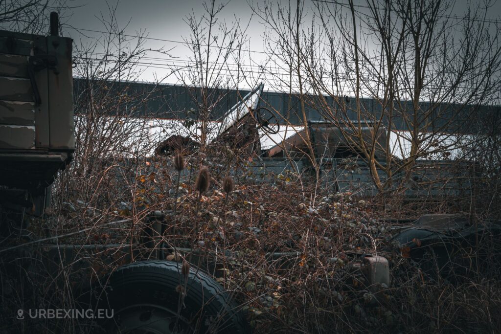a photo of a military car sitting on the trailer bed of a military truck in an abandoned vehicle storage