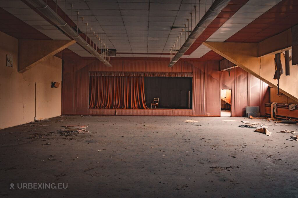 a photo of a small abandoned theatre, there is a lonely chair standing on the podium