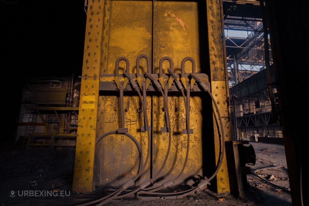 a photograph of four tools hanging from an yellowish pillar in an abandoned steel rolling mill