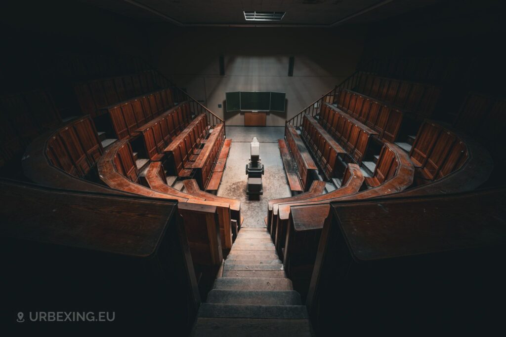 a photograph of an auditorium taken in a former medical university. the photograph shows benches, a chalk board and an old projector