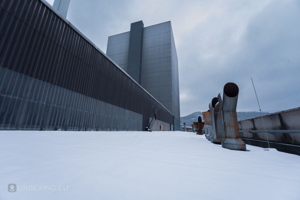 A picture of the roof of an decommisioned power plant. The picture shows airconditioning, snow and a large building.