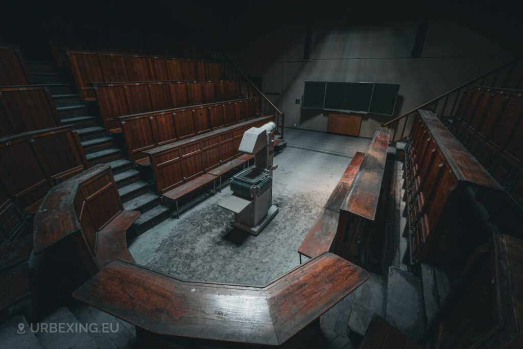 a photograph taken during urban exploring in an university auditorium. the photo shows benches, a chalk board and a vintage projector