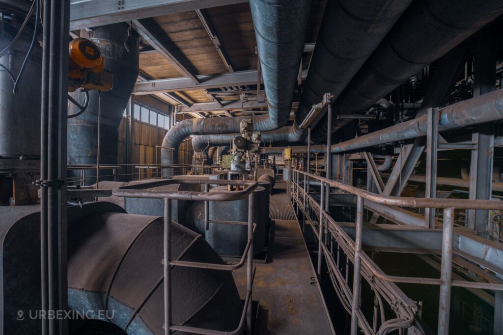 A picture inside of the boiler house at a decommisioned power plant. The picture shows some motors, tubes and other machinery.