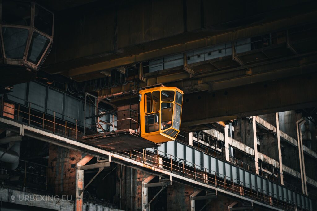 a photo of a crane with a bright yellow cabin; the crane is hanging in a former power plant called kraftwerk b