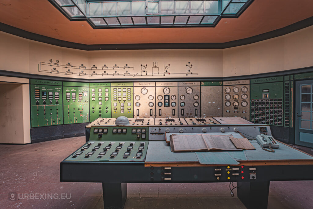 a photograph of the control room at the kraftwerk p power plant in plessa. the control room has books, a phone and many buttons