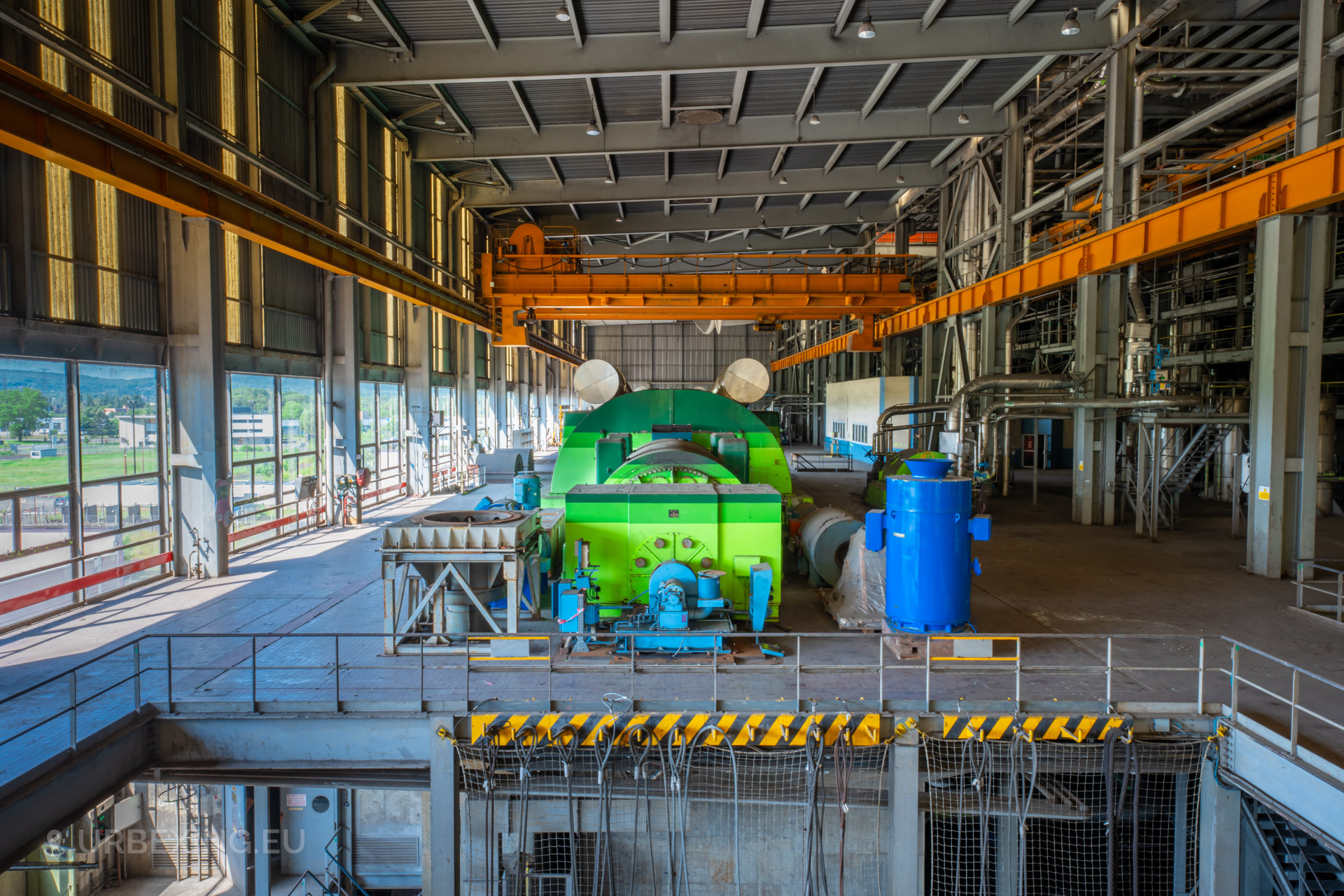 a photograph of a green turbine in an abandoned power plant. the photograph shows the turbine hall, machinery and a crane.