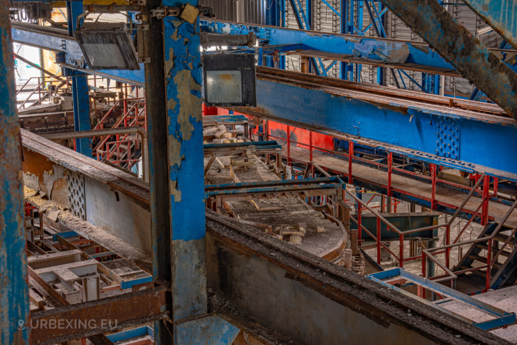 a photograph taken inside an abandoned glass factory called "de glasfabriek schiedam". The photograph is taken from the ceiling and shows a transporting system for hot glass.