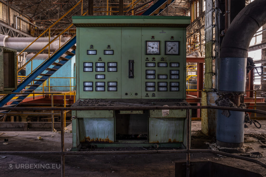 a photograph taken in at an urbex location called blue power plant. the photograph shows a control panel in the turbine hall. the panel is colored green and has multiple meters.