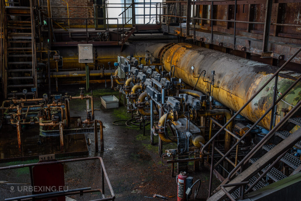 a photograph taken in at an urbex location called blue power plant. the photograph shows several small pipes for gas, colored in yellow and a large pipe for gas from the creation of cokes.