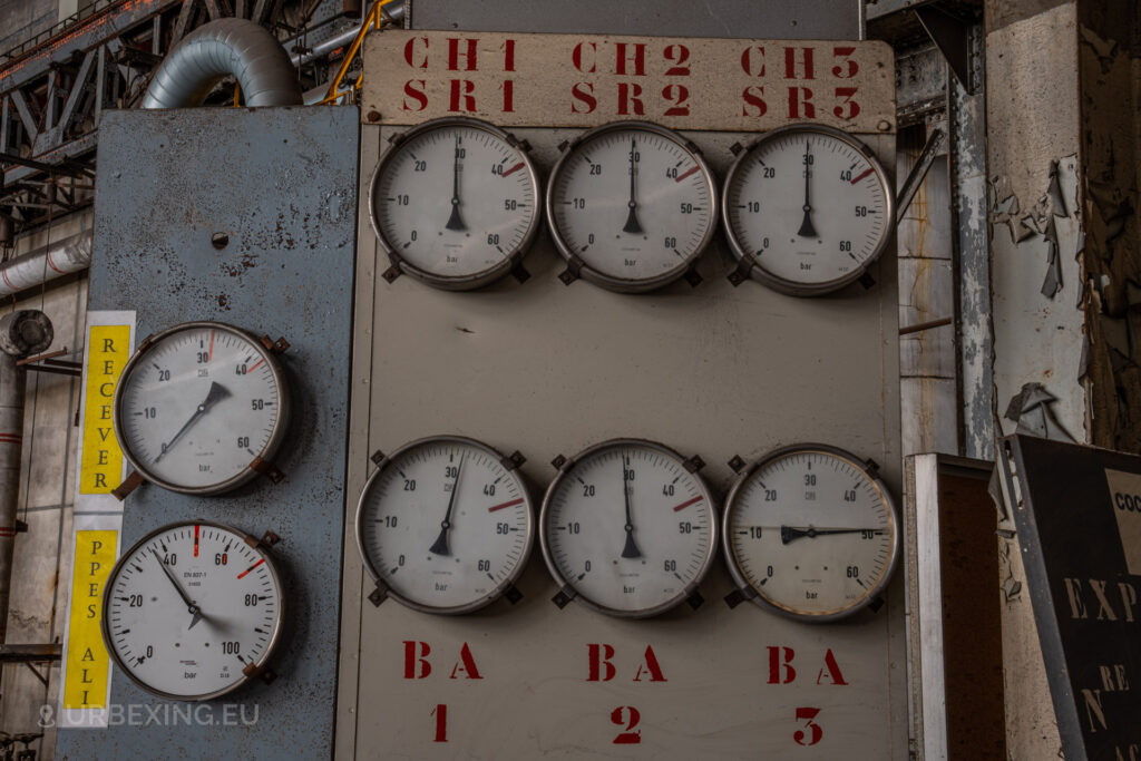 a photograph taken in at an urbex location called blue power plant. the photograph shows a panel with several pressure meters, one filled with water.