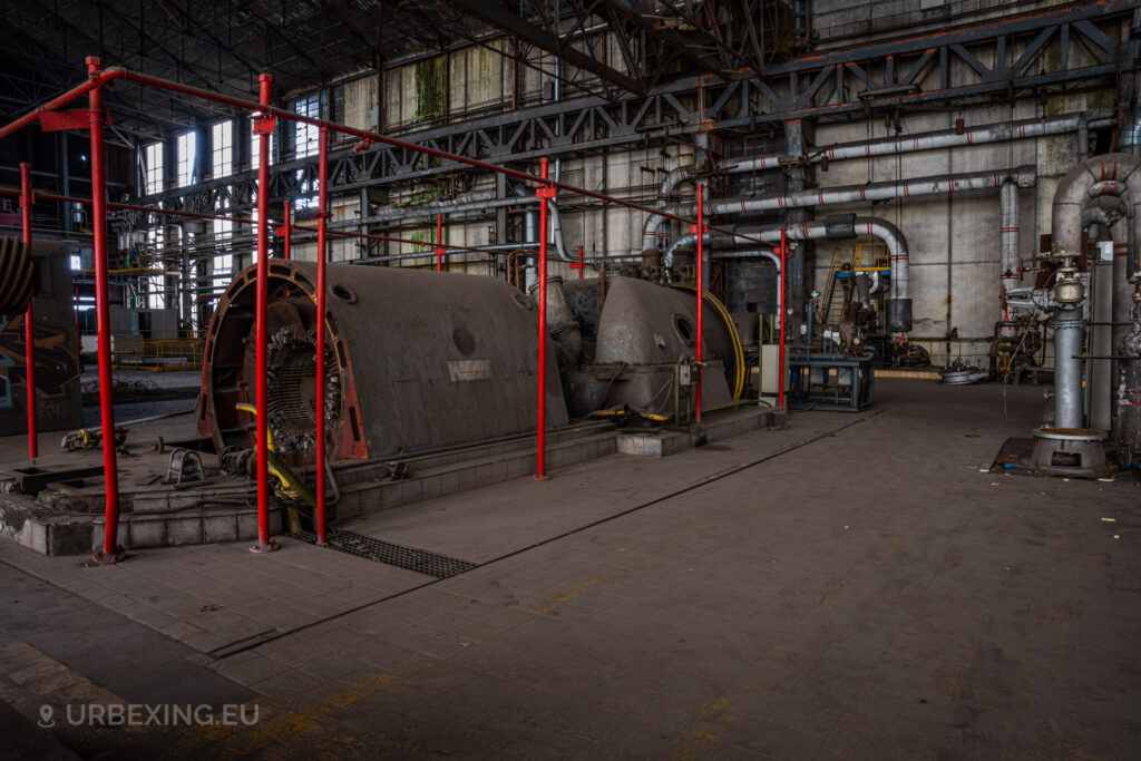 a photograph taken in at an urbex location called blue power plant. the photograph shows a small steam turbine with a red alternator. the railings are colored in red.