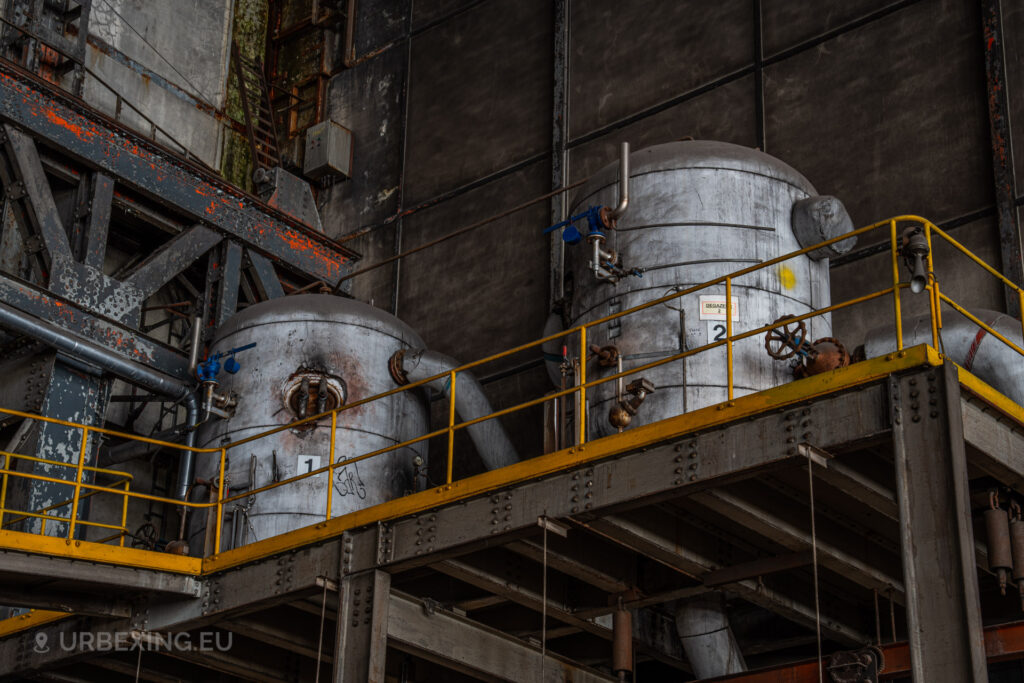 a photograph taken in at an urbex location called blue power plant. the photograph shows two small gas deaerators. the tanks are colored in white and the railings are colored in yellow.