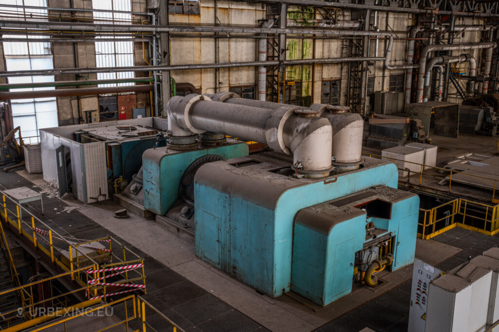 a photograph taken in at an urbex location called blue power plant. the photograph shows a blue steam turbine from the left side. the railings are covered in yellow.
