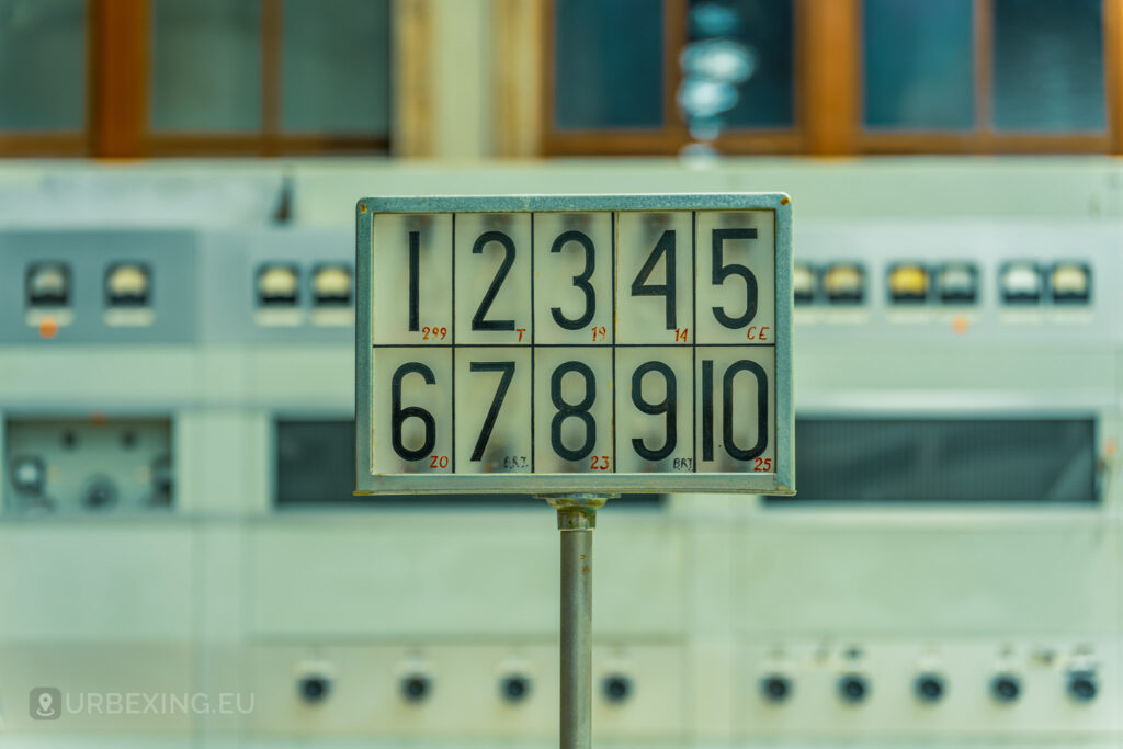 Close-up of a numbered display panel in an abandoned radio transmitting facility, with the numbers 1 to 10 prominently visible. The background features more control panels and industrial equipment, emphasizing the abandoned and neglected state of the Lost Frequencies site.