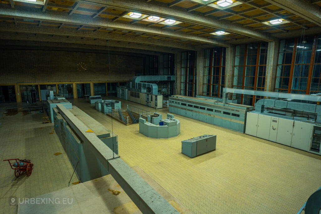 A wide-angle view of the abandoned control room at "Lost Frequencies," featuring a central control desk surrounded by various control panels and gauges. The room's industrial architecture and large windows provide a haunting backdrop, ideal for urban exploration photography.