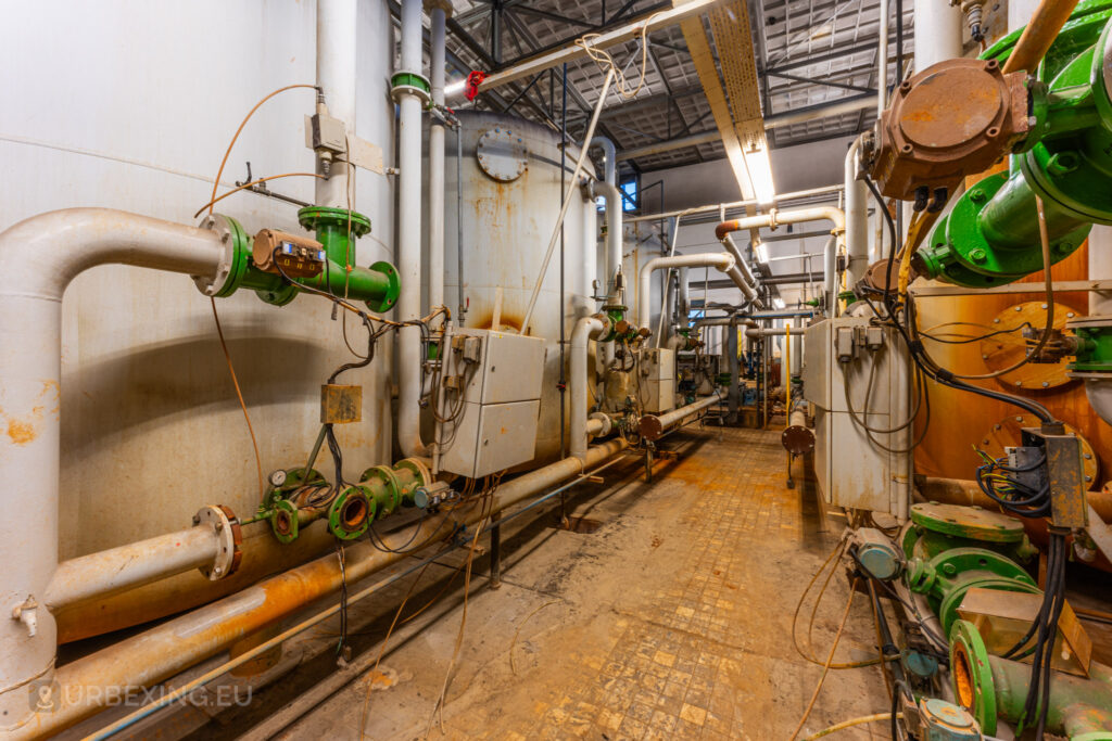 A detailed view of the intricate network of pipes and valves inside the abandoned EMGO factory in Lommel, Belgium, showcasing the complex water treatment system amidst the factory's derelict state.