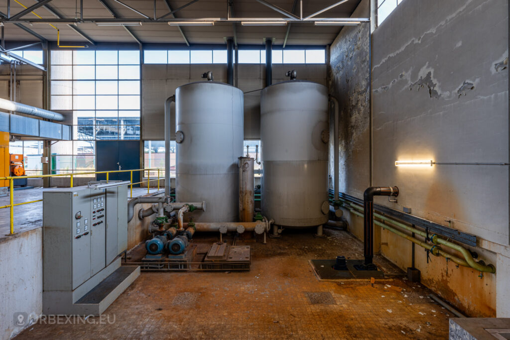 The abandoned EMGO factory in Lommel, Belgium, featuring decaying industrial tanks and control panels, reflecting its rich history in the glass and lighting industry.