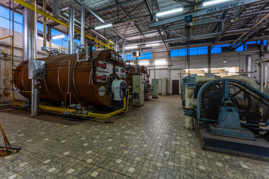 The abandoned EMGO factory in Lommel, Belgium, features large rusted water treatment tanks and extensive industrial machinery, highlighting the factory's historical significance and current state of decay.