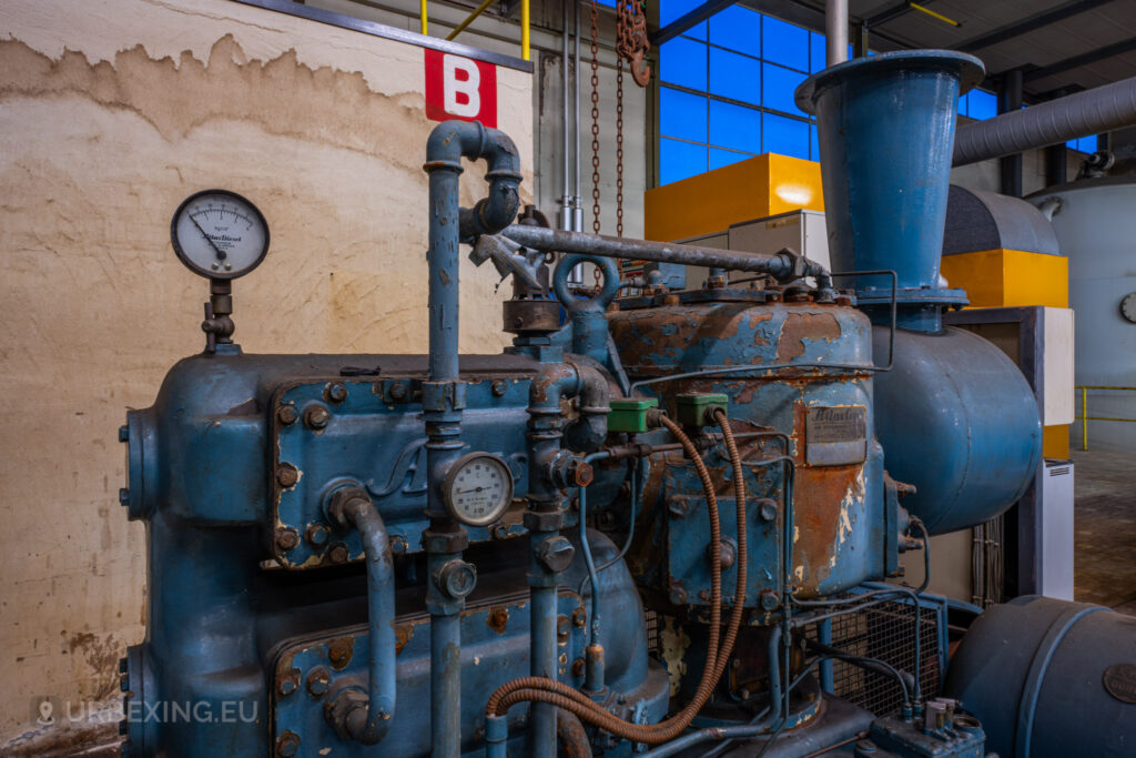 A close-up of an Atlas Copco machine in the abandoned EMGO factory in Lommel, Belgium, showcasing the intricate details and rusted components of the industrial equipment amidst the decayed setting.