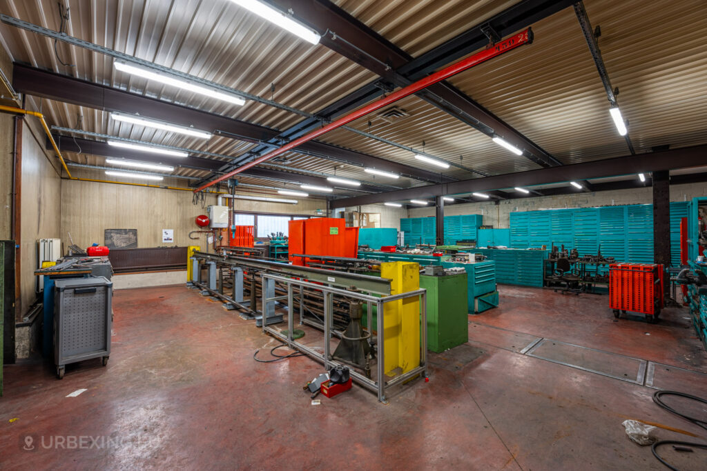 Spacious workshop area in the abandoned Ateliers de La Meuse, Liège, Belgium, featuring colorful tool cabinets, metal workstations, and fluorescent lighting illuminating the industrial space.