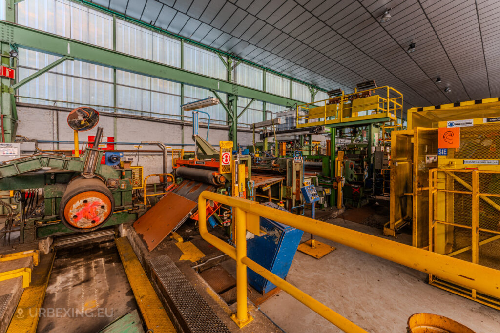 Abandoned industrial workspace with vibrant yellow railings and machinery at the ArcelorMittal Marchin plant in Liège, Belgium.