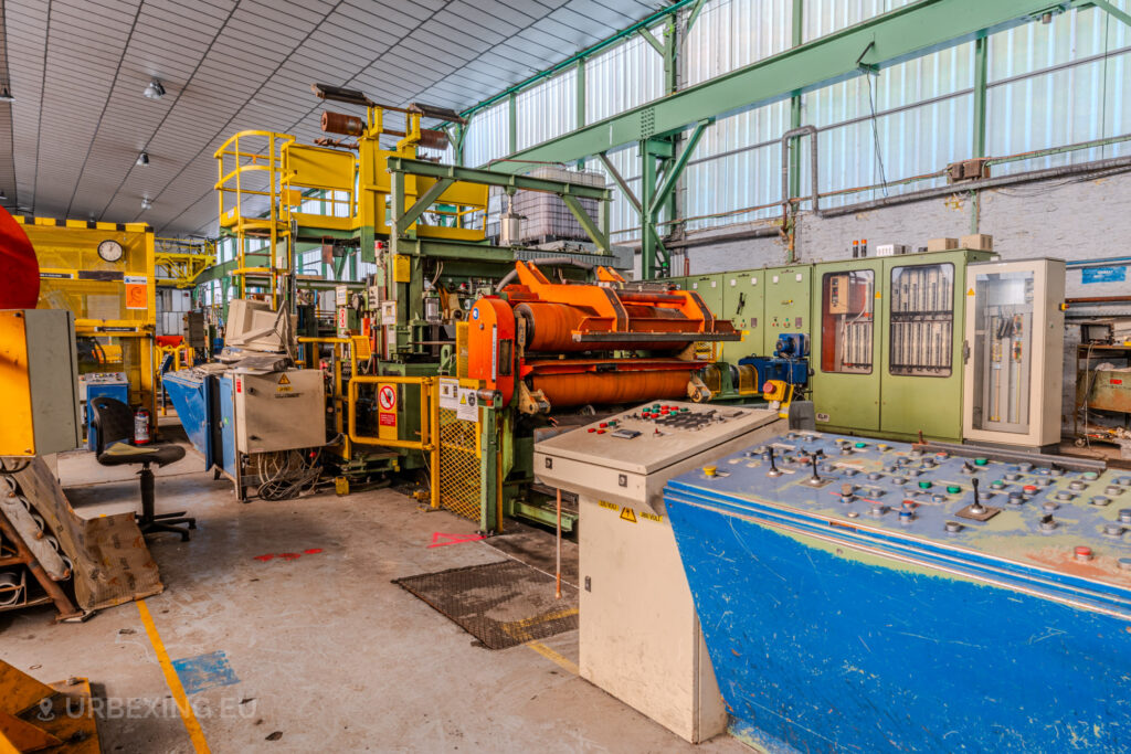 Abandoned industrial workstation with colorful machinery, control panels, and equipment inside the ArcelorMittal Marchin plant in Liège, Belgium.