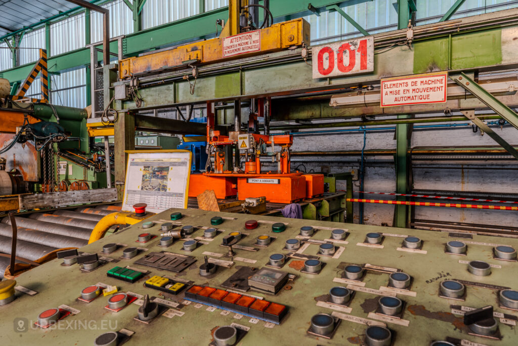 Close-up of a control panel with colorful buttons and an orange industrial machine at the abandoned ArcelorMittal Marchin plant in Liège, Belgium.