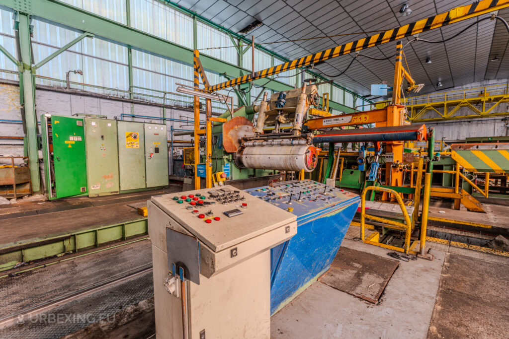 Control panel and industrial rollers inside the abandoned ArcelorMittal Marchin plant in Liège, Belgium, surrounded by vibrant green and yellow equipment.