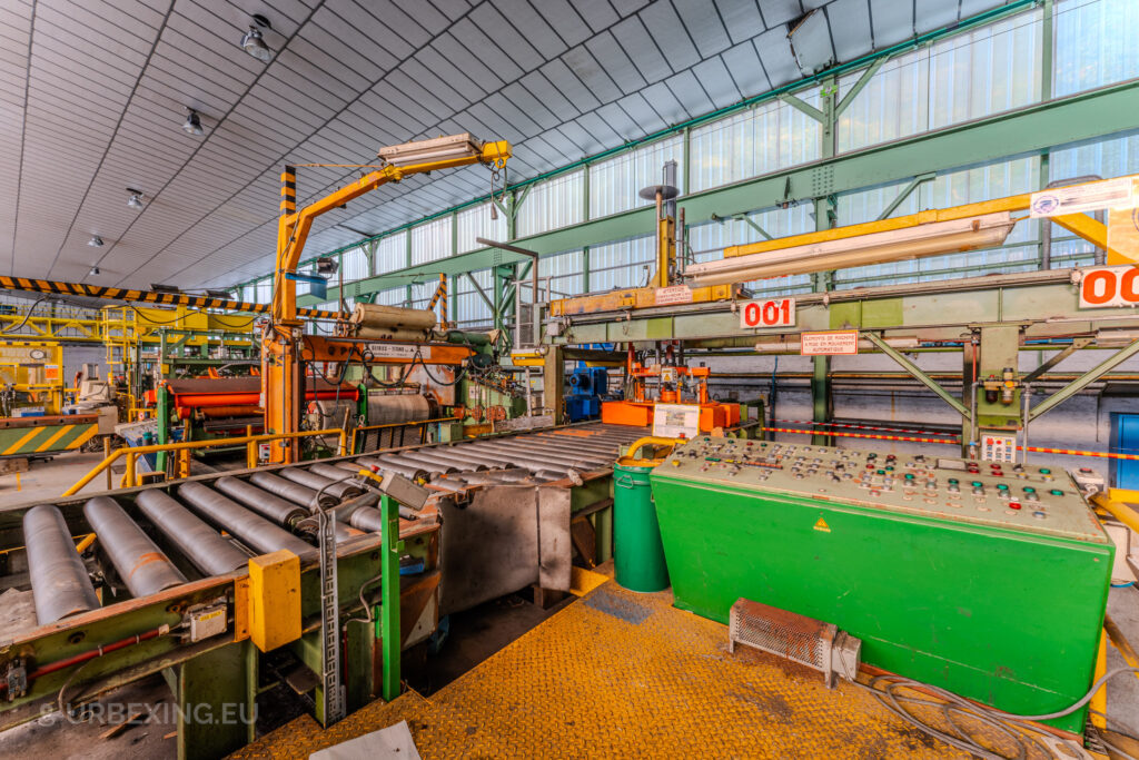 Close-up of machinery and control panels inside the abandoned ArcelorMittal Marchin plant in Liège, Belgium, showcasing green, orange, and yellow equipment.