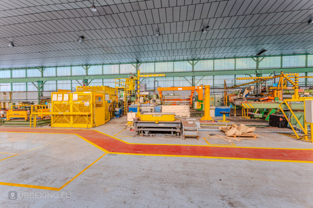 Industrial floor with yellow machinery and vibrant red safety markings at the abandoned ArcelorMittal Marchin plant in Liège, Belgium.