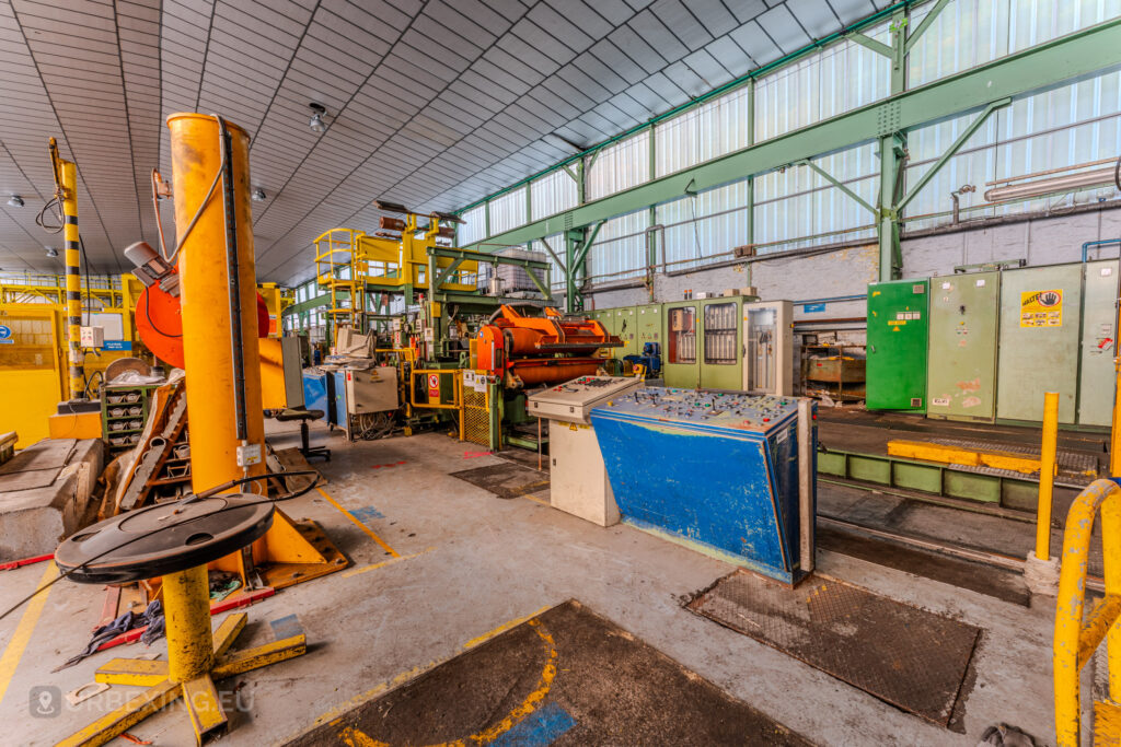 Industrial workstation with yellow, blue, and orange machinery inside the abandoned ArcelorMittal Marchin plant in Liège, Belgium.