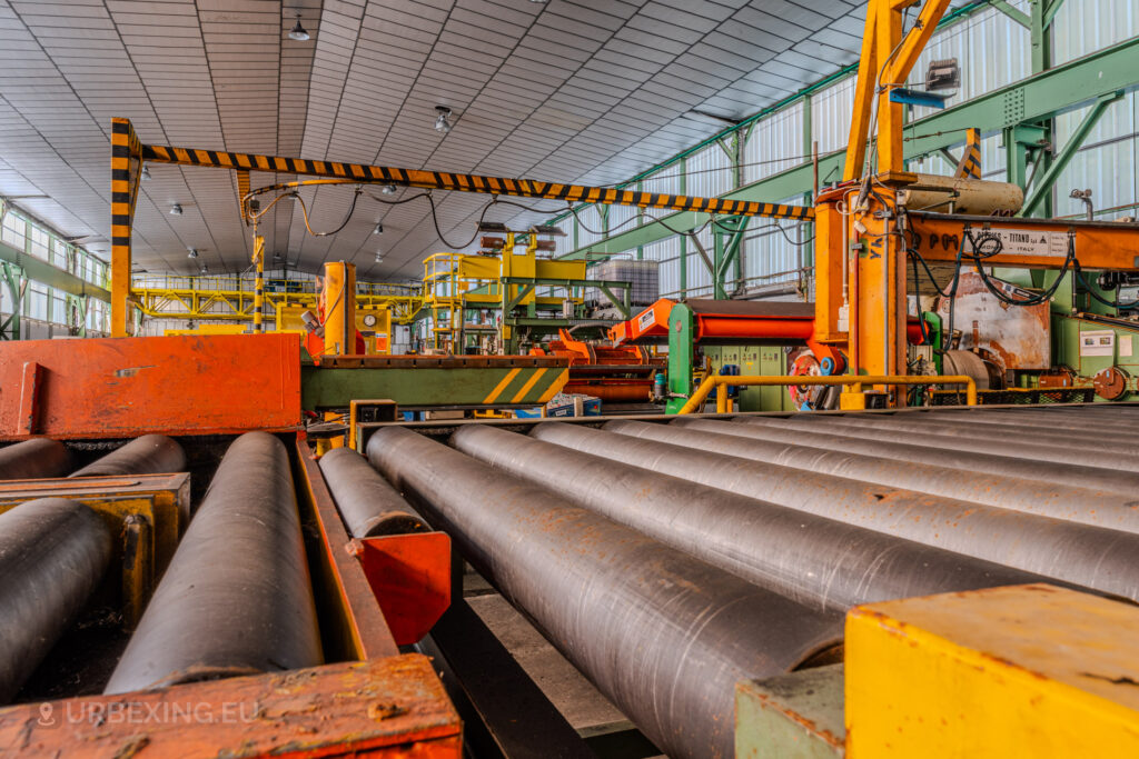 Rusty rollers and machinery inside the abandoned ArcelorMittal Marchin plant in Liège, Belgium, with bright yellow and orange industrial equipment.