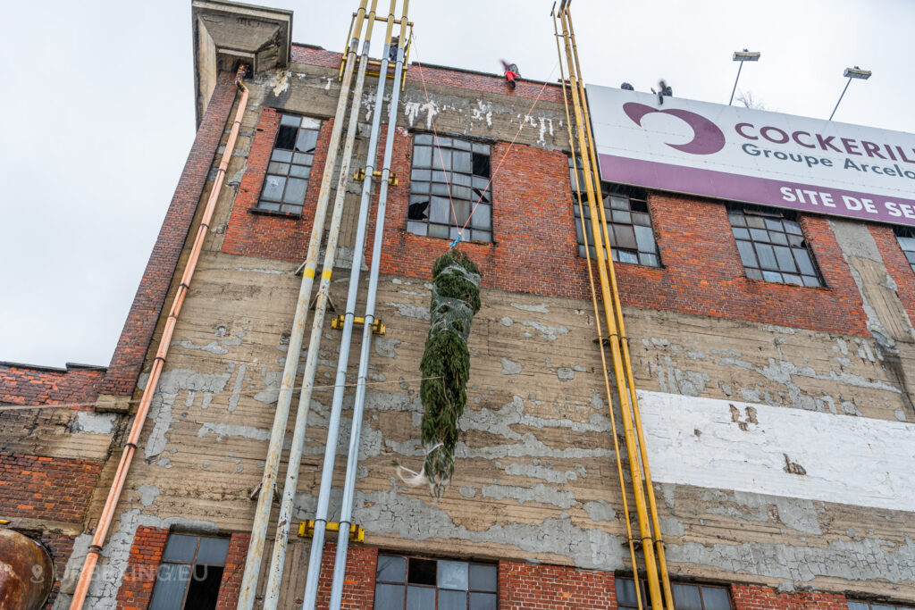 A Christmas tree is carefully hoisted up the facade of the abandoned HF6 power plant in Seraing, Belgium, showcasing a festive twist amidst the industrial decay during this urban exploration adventure.