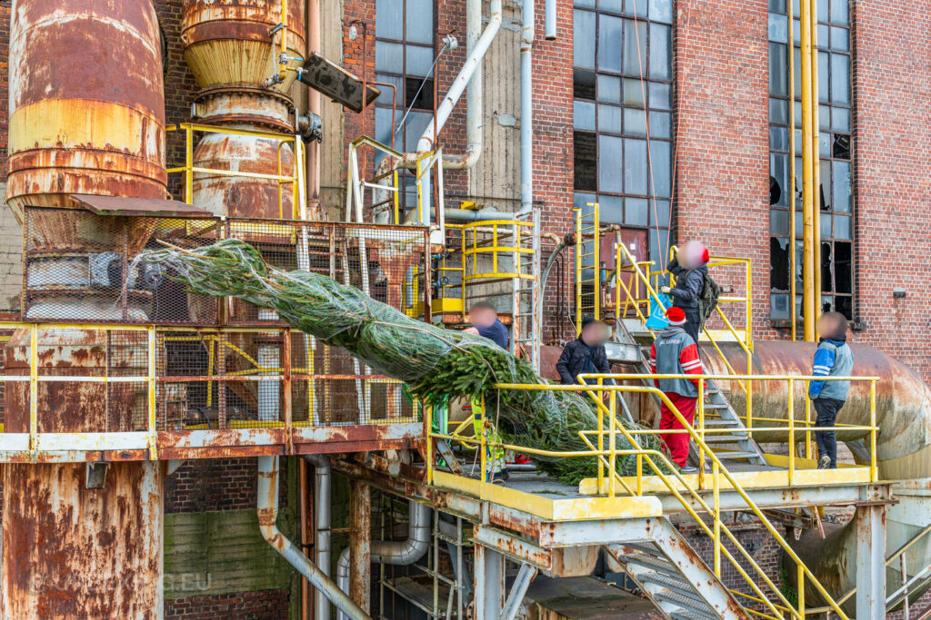 A group of urban explorers carefully situates a Christmas tree on a rusted industrial platform at the abandoned HF6 power plant in Seraing, Belgium, combining holiday festivity with the gritty aesthetic of urban exploration.