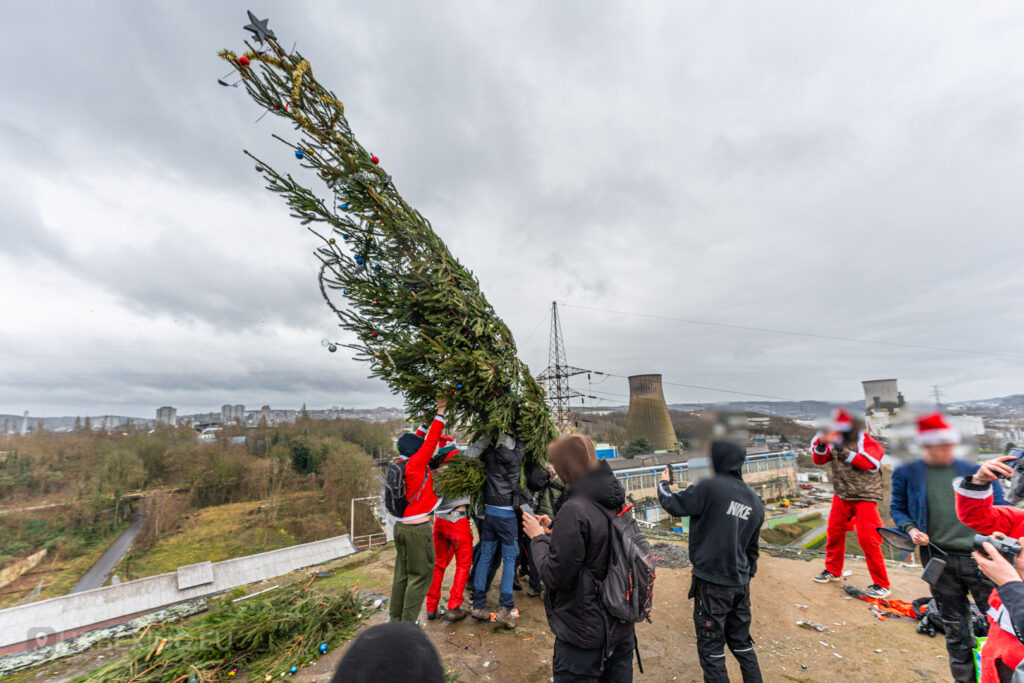 Urban explorers collaborate to erect a decorated Christmas tree on the rooftop of the abandoned HF6 power plant in Seraing, Belgium, blending holiday festivities with the rugged charm of urban exploration.