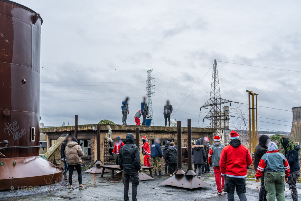 Urban explorers gather on the rooftop of the abandoned HF6 power plant in Seraing, Belgium, surrounded by industrial relics and a gloomy sky, epitomizing the adventurous spirit of urban exploration.