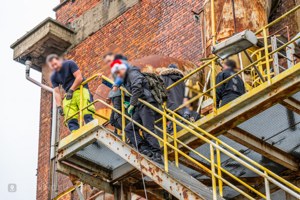 Urban explorers climb a rusted staircase at the abandoned HF6 power plant in Seraing, Belgium, combining industrial decay with festive touches during their adventure.