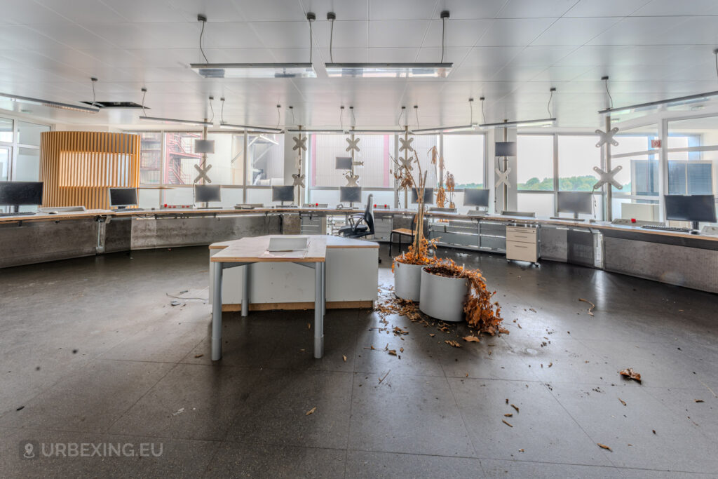 Abandoned control room inside the former Kraftwerk Voerde in Voerde, Germany, with decaying desks, dead plants, and scattered debris.