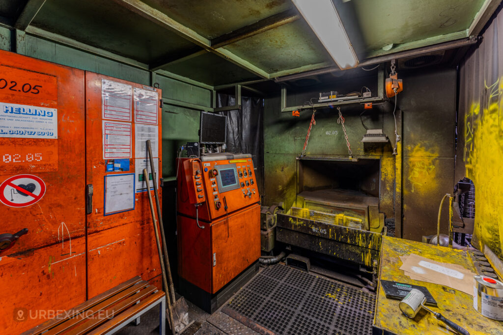 Detail of a control station and machinery in the Vallourec steel mill in Düsseldorf-Rath, with bright orange and yellow equipment showing signs of wear and industrial decay.