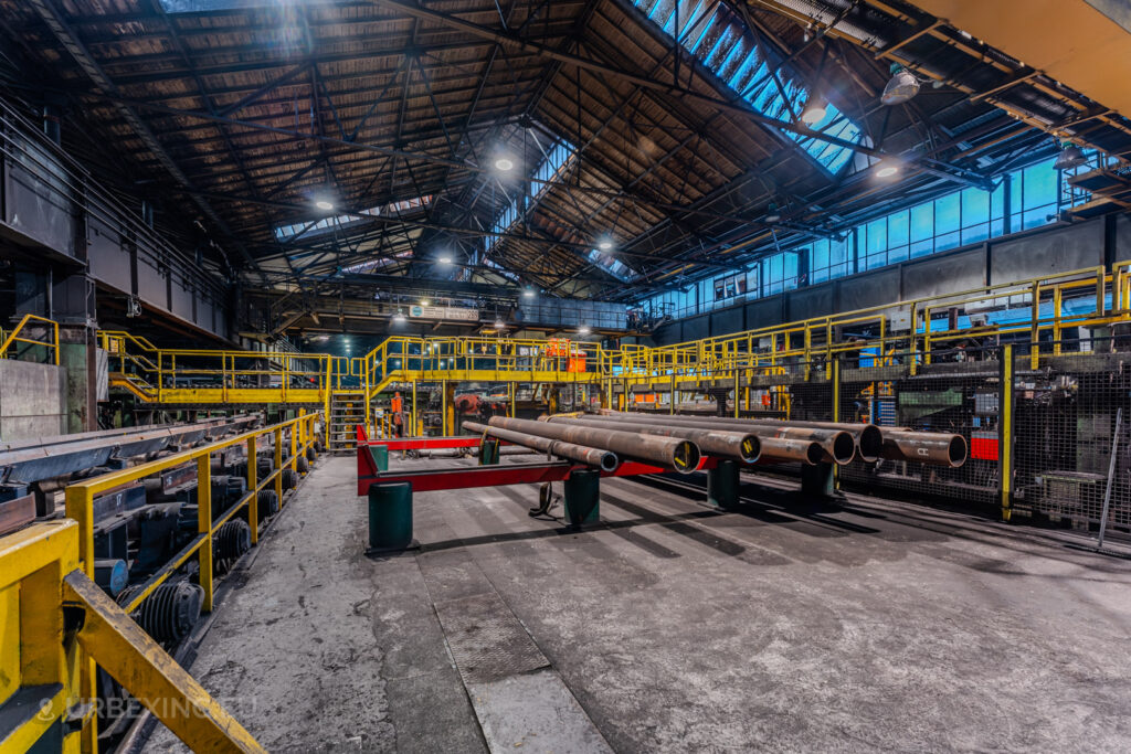 Abandoned steel production area at the Vallourec steel mill in Düsseldorf-Rath, featuring steel tubes on support beams and a backdrop of industrial railings and machinery.”