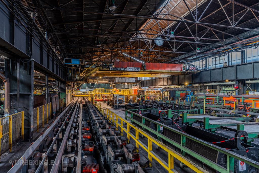 Production floor of the abandoned Vallourec steel mill in Düsseldorf-Rath, with industrial machinery, steel tracks, and overhead cranes, encapsulating the legacy of steel tube manufacturing.