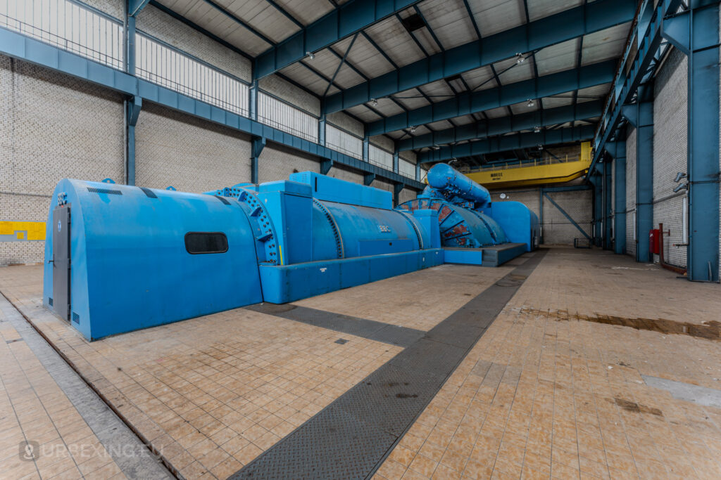 Angled view of a blue BBC turbine generator in the abandoned Kraftwerk Voerde, Voerde, Germany, showcasing industrial decay.