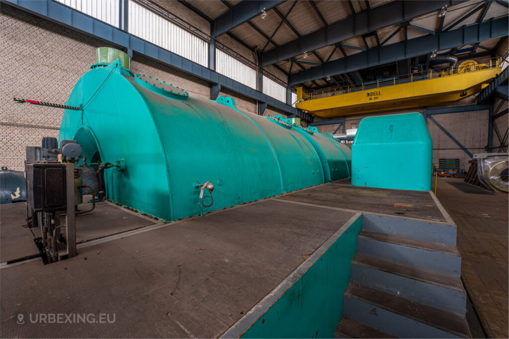 Close-up of the turquoise housing of a turbine in the abandoned Kraftwerk Voerde, Voerde, Germany, with a yellow overhead crane visible.