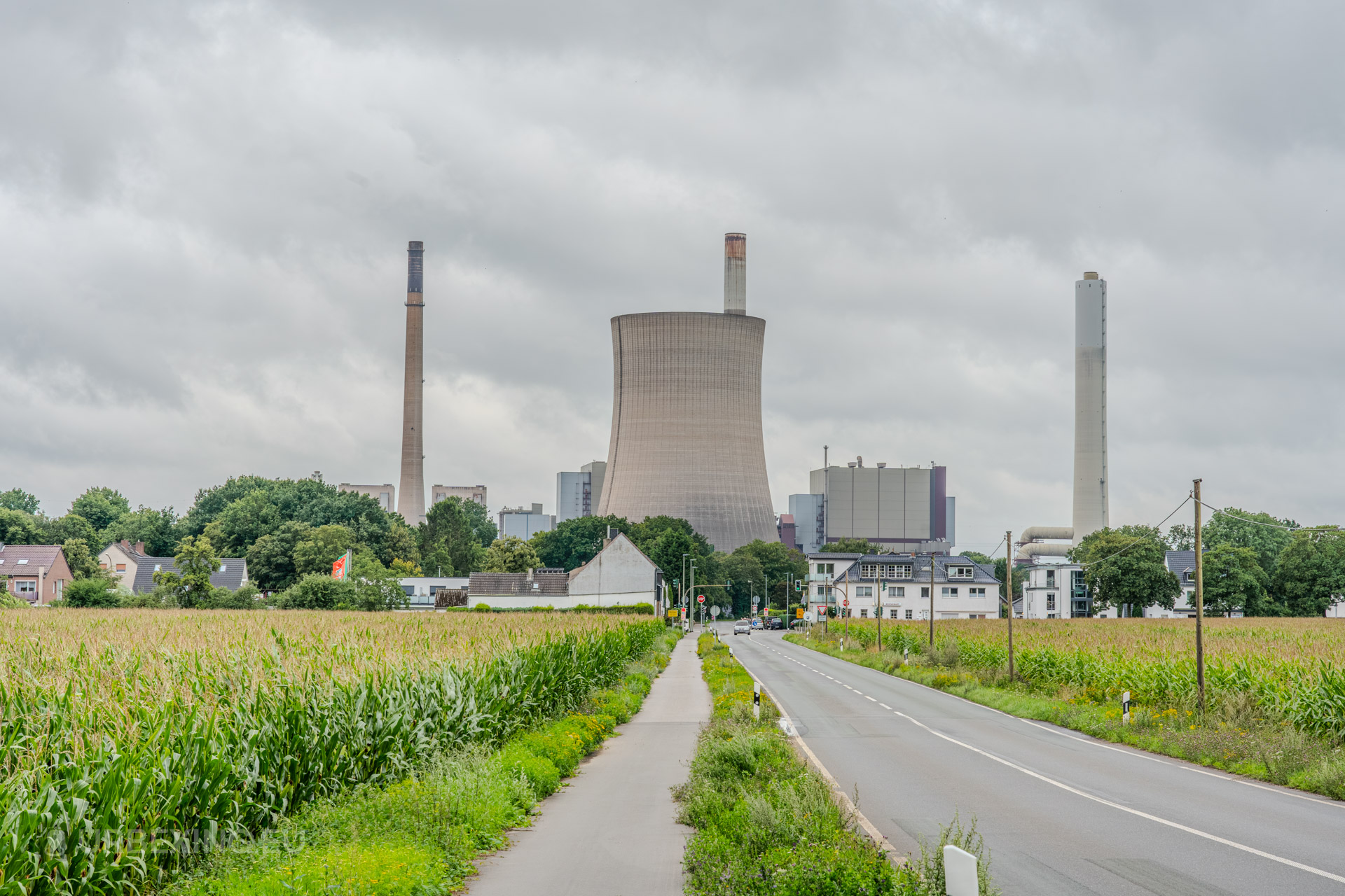 Exterior view of the Kraftwerk Voerde power plant in Voerde, Germany, with towering chimneys and a cooling tower surrounded by greenery and houses.