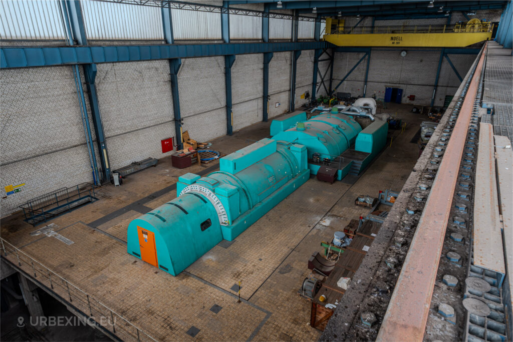 Overhead view of a turquoise generator with an orange door in the abandoned turbine hall of Kraftwerk Voerde, Germany.