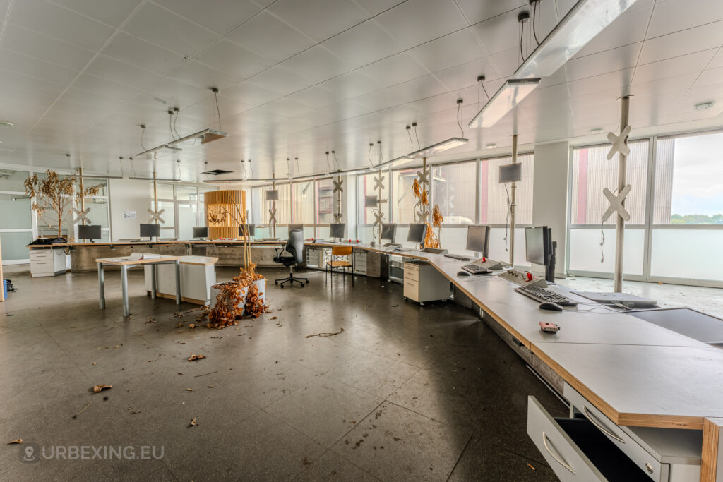 Wide view of the abandoned control room at Kraftwerk Voerde in Voerde, Germany, with empty desks, dead plants, and debris on the floor.